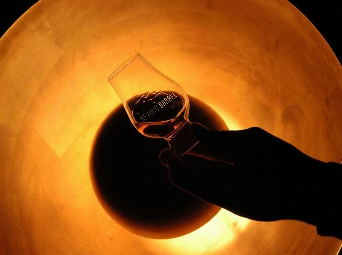 A Beyond Barrel tasting glass held to warm light